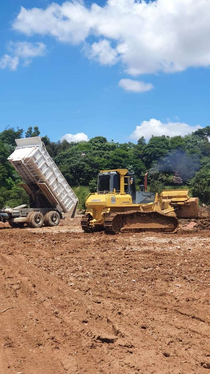 Caminhão basculante descarregando e trator de esteira espalhando o material na frente do aterro