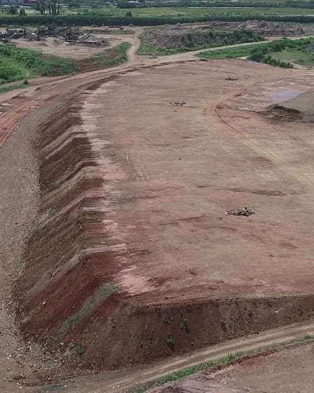 Bancada de corte da cava do aterro, em degraus de terra vermelha, com as vias de acesso ao redor